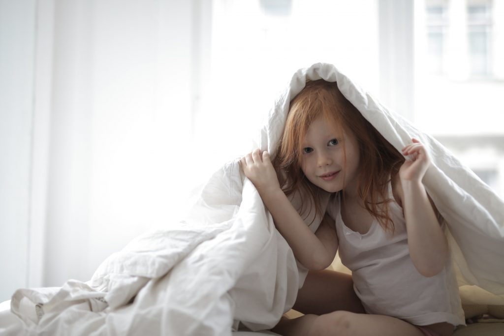 Petite fille qui se cache sous sa couette de lit